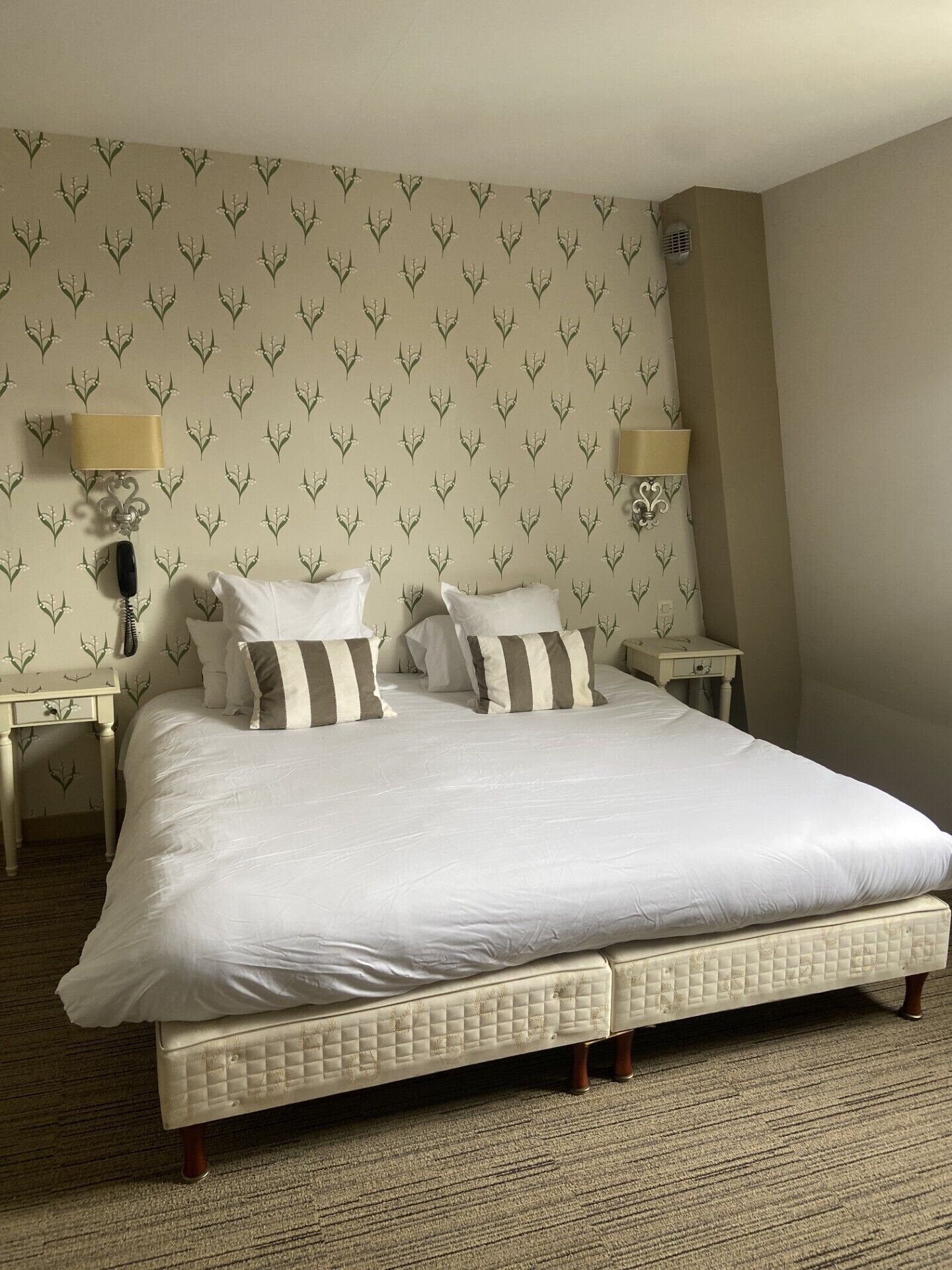 Un grand lit avec une tête de lit matelassée, deux tables de chevet avec des lampes et un papier peint à motifs.