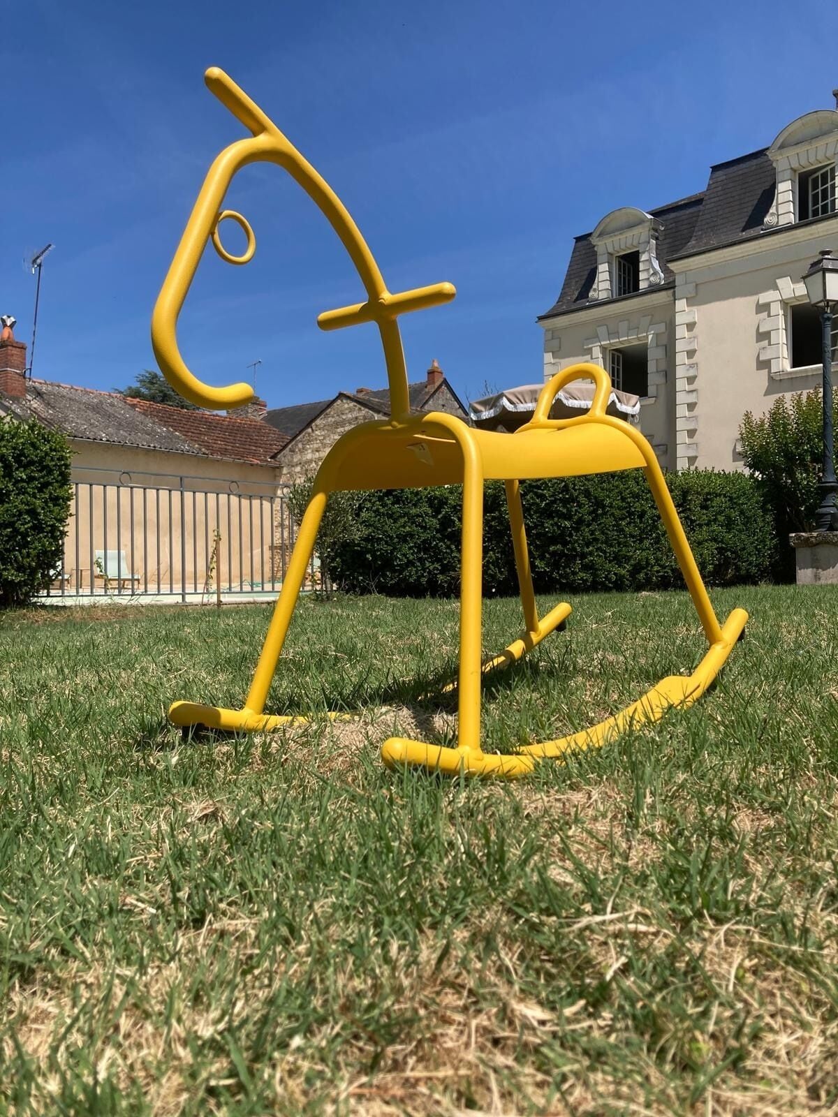 A yellow rocking horse in a grassy area with a house in the background.