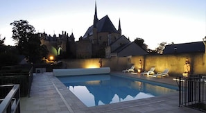 A swimming pool with lounge chairs, a castle-like building in the background, and a stone pathway leading to the pool.