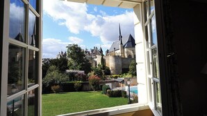 A view from a window overlooking a castle with a well-maintained lawn and a swimming pool.