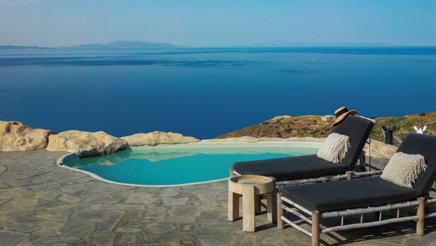 A poolside area with lounge chairs and a stone-tiled floor, overlooking a large body of water and distant mountains.