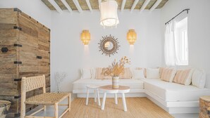 A modern living room with a white sofa, wooden accent wall, two wall-mounted lights, a round coffee table, and a woven chair.