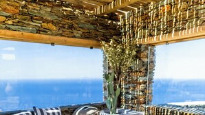 A sunlit outdoor seating area with stone walls, a view of the sea, and a stone floor.