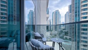 A balcony with two chairs and a small table, overlooking a cityscape with tall buildings. - ACTONE Tower2-Step to Burjkhalifa-1BR (Dubai)