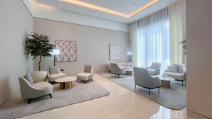 A modern living room with a large window, a potted plant, and multiple seating areas. - ACTONE Tower2-Step to Burjkhalifa-1BR (Dubai)
