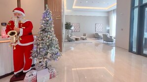 A modern hotel lobby with a large Christmas tree, a person in a Santa suit playing a saxophone, and a seating area with contemporary furniture. - ACTONE Tower2-Step to Burjkhalifa-1BR (Dubai)