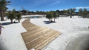 A wooden boardwalk leading to a pool area with palm trees and a clear blue sky. - CAMPING 5 🌟MOBIL HOME RENTAL PREMIUM GAME AT VALRAS BEACH (Valras-Plage)