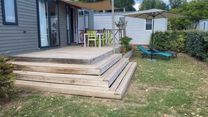 A modern house with a wooden deck, a covered patio, outdoor seating, and a well-maintained garden. - CAMPING 5 🌟MOBIL HOME RENTAL PREMIUM GAME AT VALRAS BEACH (Valras-Plage)