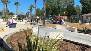 A playground with a slide and climbing structures, surrounded by palm trees and a clear blue sky. - CAMPING 5 🌟MOBIL HOME RENTAL PREMIUM GAME AT VALRAS BEACH (Valras-Plage)