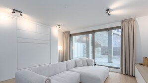 A modern living room with a large sectional sofa, a round coffee table, and a large window with curtains. - Newly Built Studio on 1st Floor With Terrace (Middelkerke)