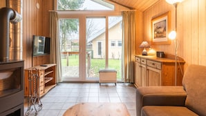 A cozy living room with a wooden interior, a fireplace, a TV, and a large sliding glass door leading to a backyard. - Ferienhaus mit Sauna im Ferienpark Mirow (Mirow)
