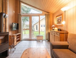 Un salon chaleureux avec un décor intérieur en bois, une cheminée, un téléviseur et une grande porte-fenêtre coulissante donnant sur un jardin.