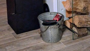 Een moderne haard met een glazen ombouw, een metalen emmer en gestapelde houtblokken.