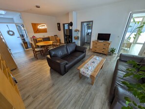 Un salon moderne avec un canapé en cuir, une table basse en bois, un coin repas et un téléviseur.