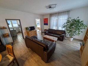 Un salon avec un canapé, une table basse, un téléviseur et une grande plante.