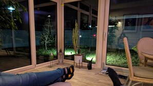 Een kamer met grote ramen, een bank, een stoel en een kleine tafel.