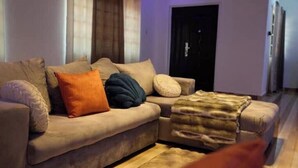Een woonkamer met een bank, kussens en een plaid.