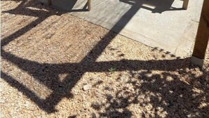 Un patio con mobiliario de madera, incluyendo sillas y una mesa, bajo una pérgola.