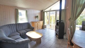 Una sala de estar acogedora con un sofá, una mesa de centro de madera, una zona de cocina con estufa y un ventanal corredero que da a un jardín.