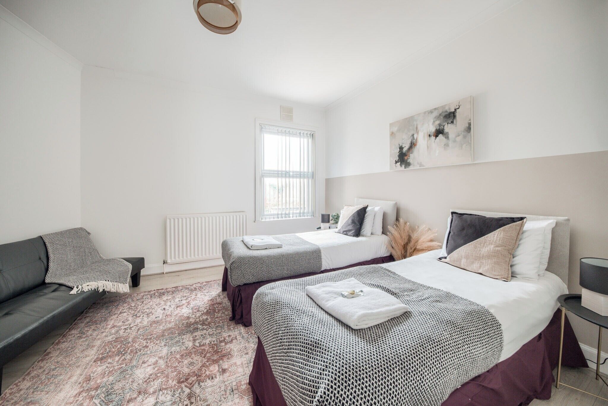 A modern bedroom with two beds, a sofa, and a large window.
