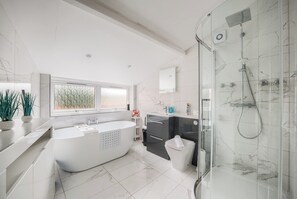 Un baño moderno con una bañera independiente, ducha con mampara de vidrio y un amplio ventanal que proporciona luz natural.