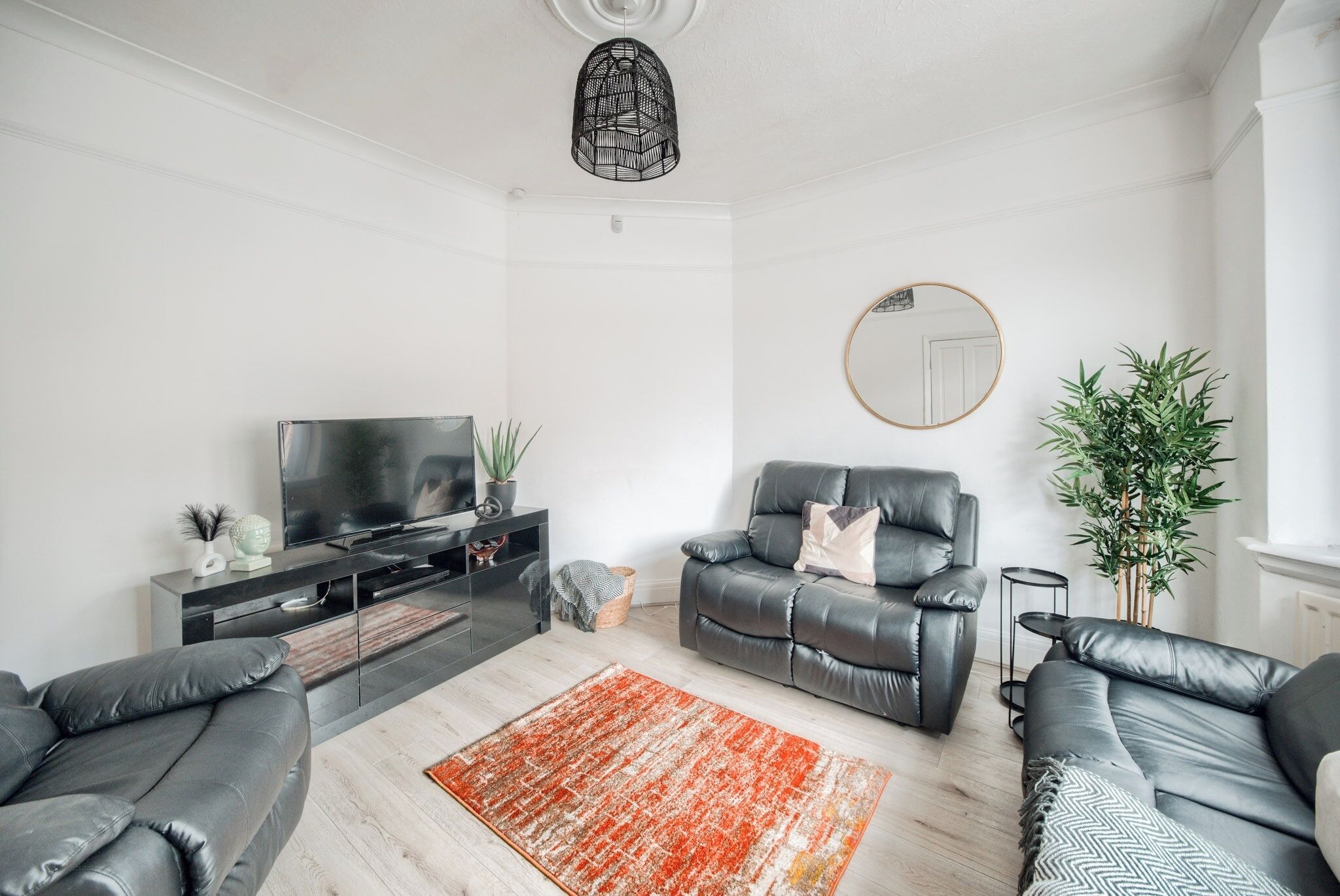 A modern living room with a flat-screen TV, leather sofas, a coffee table, a red rug, and a large mirror.