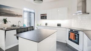 A modern kitchen with white cabinetry, a black countertop island, a built-in oven, and a stainless steel range hood. - Sleeps7-pet&familyfriendly With Parking (Coventry)