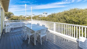 A wooden deck with a white table and chairs, surrounded by a white railing, overlooking a coastal area with houses and dense foliage. - Beachside in Seaside, FL, 3 King Suites, Amazing Gulf Views - 2 Adult Bikes! (Santa Rosa Beach)