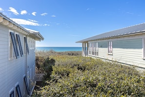 A coastal house with a view of the ocean, surrounded by dense shrubbery.