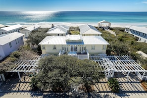 Une propriété située sur la côte, comprenant plusieurs bâtiments, une grande maison principale dotée d’un balcon et offrant une vue sur la plage.