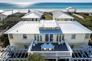 A large house with a covered patio, white railings, and a view of the ocean.