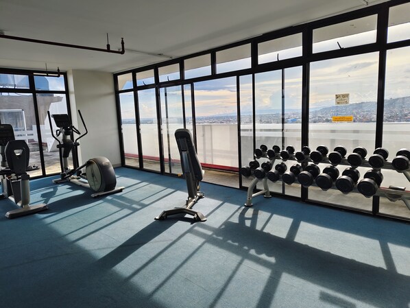 A gym with exercise equipment and a view of a cityscape through large windows.