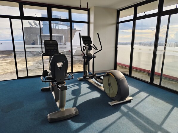 Un gimnasio con equipo de ejercicio y amplios ventanales que ofrecen vistas a la ciudad.