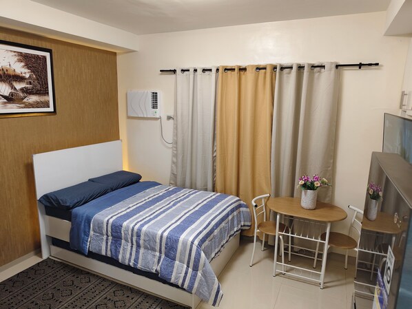 A neatly arranged bedroom with a bed, a small table with chairs, a TV, and a wall-mounted air conditioner.