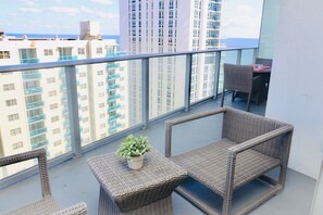 Ein Balkon mit Korbmöbeln, einem Blumentopf und Blick auf hohe Gebäude.