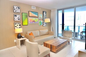 A modern living room with a beige sofa, a wooden coffee table, and a large window with a city view.
