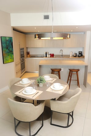 A modern kitchen with a central island, a dining table with four chairs, and a painting on the wall.