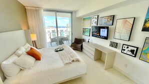 A modern hotel room with a large bed, a desk, and a balcony with a city view.