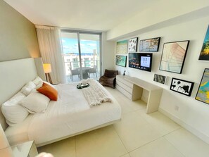 A modern hotel room with a large bed, a desk, and a balcony with a city view.