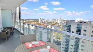 A balcony with wicker furniture, a round table, and a view of a cityscape.