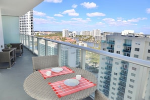 A balcony with wicker furniture, a round table, and a view of a cityscape.