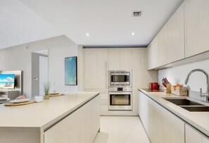 A modern kitchen with a central island, built-in appliances, and a large window.