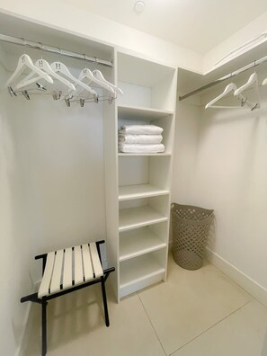 A walk-in closet with white shelves, a bench, and a laundry basket.
