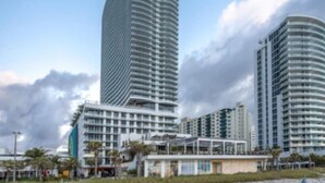 A high-rise hotel with a curved facade, multiple balconies, and a beachside location.