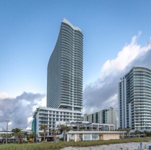 A high-rise hotel with a curved facade, multiple balconies, and a beachside location.