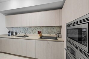 A modern kitchen with light wood cabinetry, a tiled backsplash, and a Bosch microwave oven.