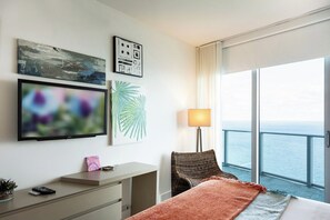 A hotel room with a bed, a desk, a chair, a TV, and a large window with a view of the sea. - Luxury 2BR/2BA Hyde Condo with Direct Beach View (Hollywood)