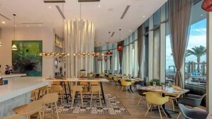 En moderne restaurant med en lang disk, flere borde og stole. Store vinduer langs den ene side lukker naturligt lys ind og giver udsigt ud.