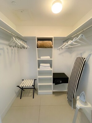 A walk-in closet with white hanging space, shelves, and a bench.