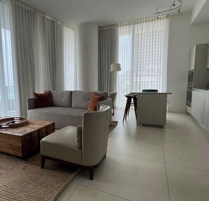 Een moderne woonkamer met een bank, fauteuil, salontafel en een klein eethoekje met een barstoel.